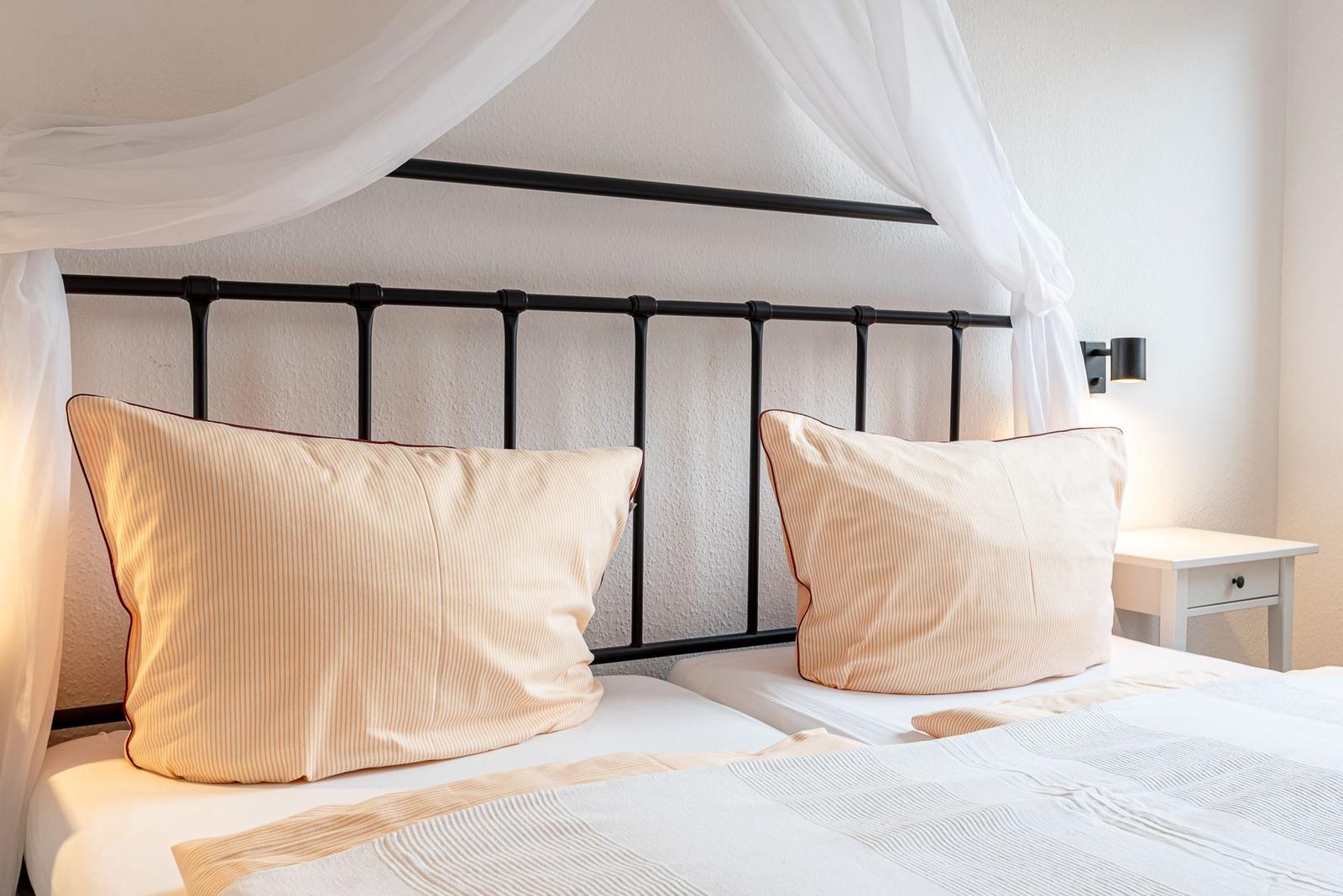 Schlafzimmer mit Bett, weißen Vorhängen und Nachttisch.