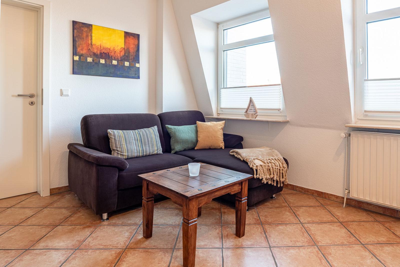 Ein Wohnzimmer mit dunklem Sofa, Holztisch und Fenstern.