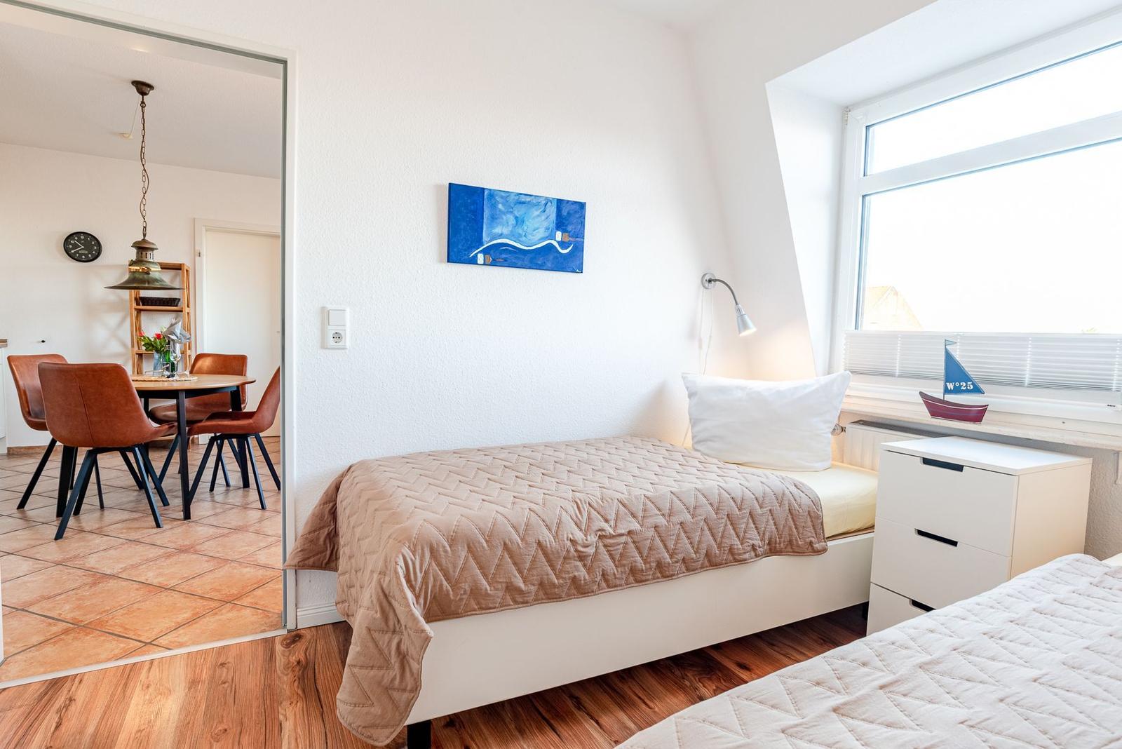 Schlafzimmer mit Bett, Nachttisch und Fenster. Durchgang zum Essbereich mit Tisch und Stühlen.