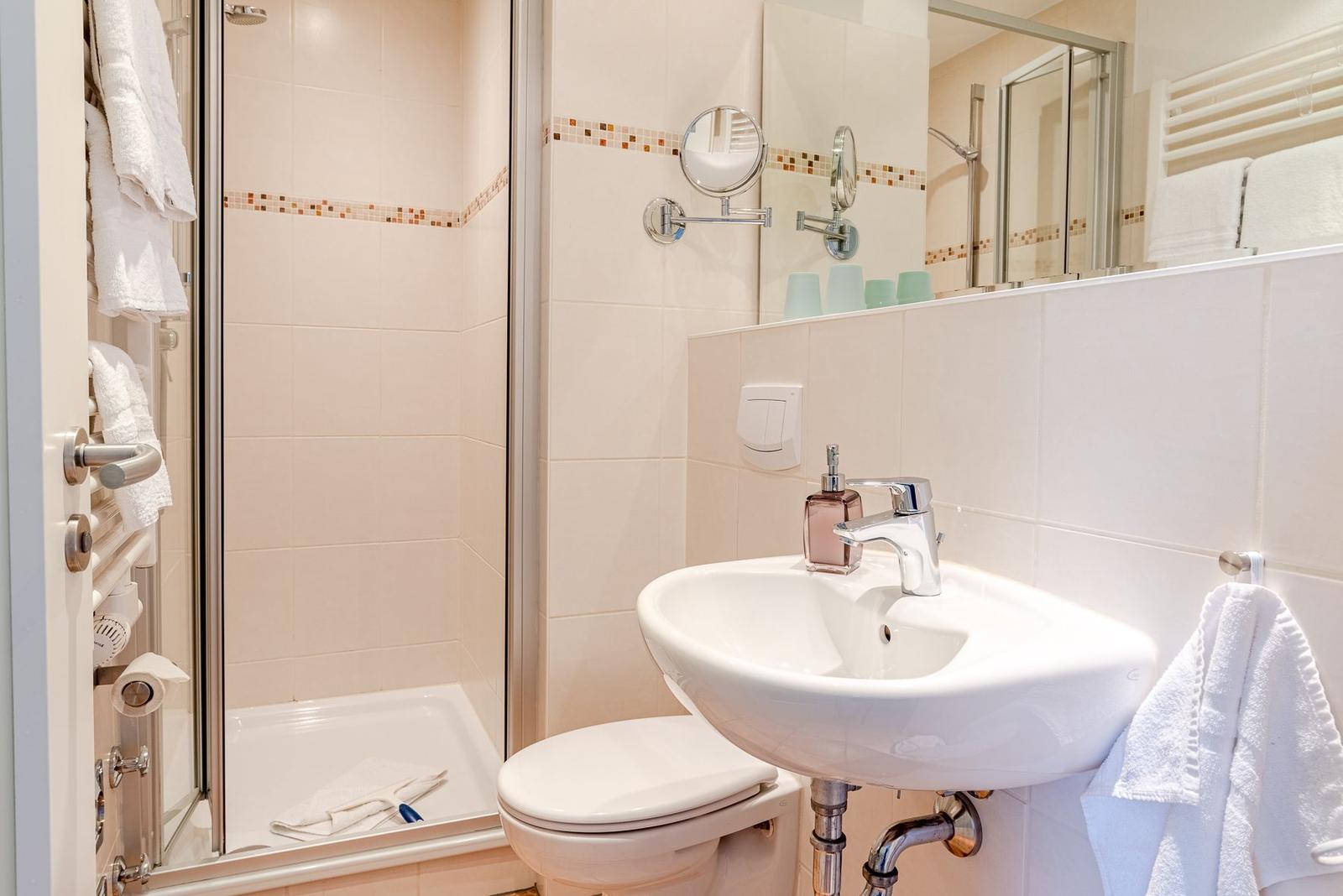 Badezimmer mit Dusche, Waschbecken und Toilette. Weiße Fliesen und Handtücher.