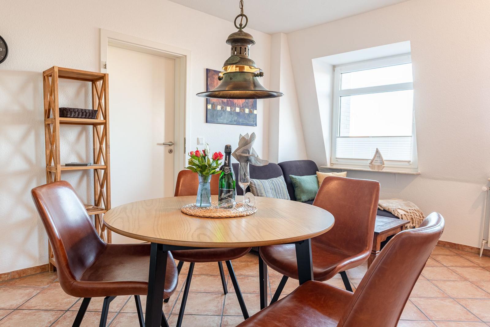 Runder Tisch mit vier braunen Stühlen, Lampe und Fenster im Hintergrund.