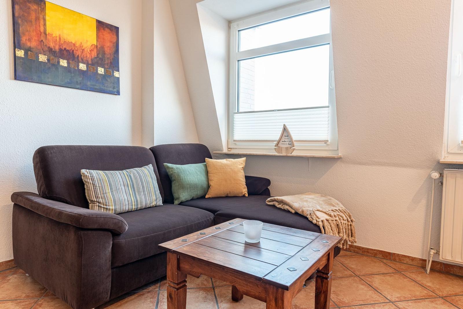 Ein Wohnzimmer mit braunem Sofa, Holztisch und Fenster. Wandbild und Deckenfenster sind sichtbar.