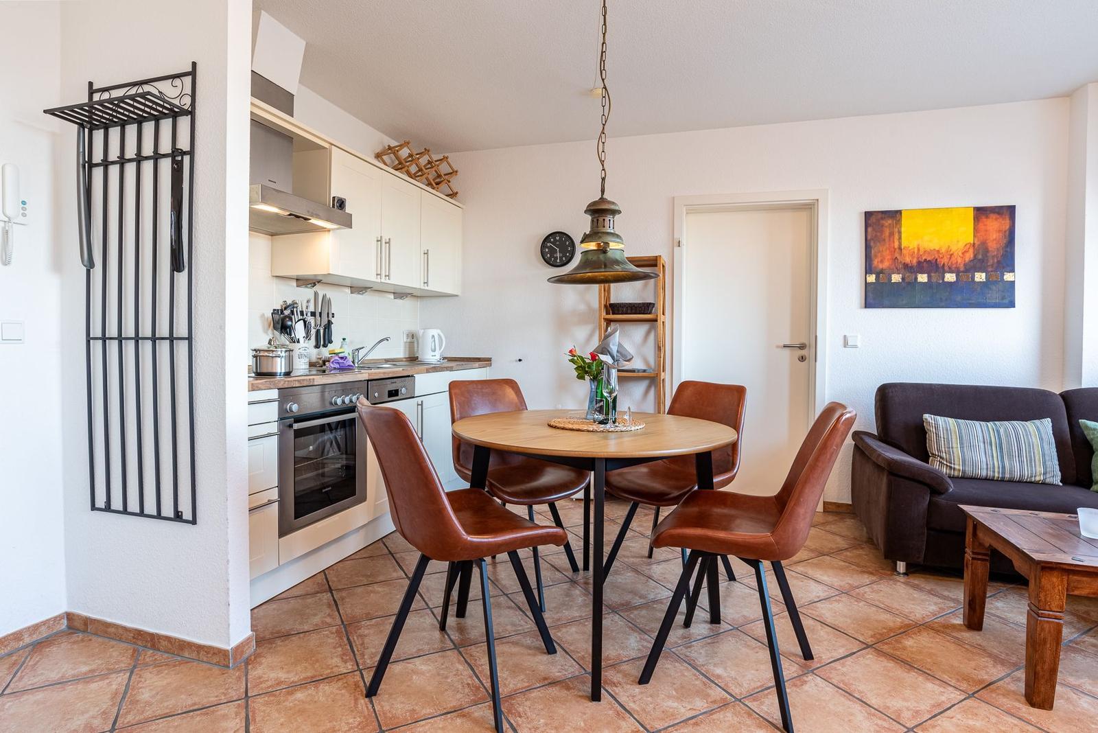 Küche mit Essbereich und Wohnzimmer. Holztisch mit vier braunen Stühlen. Sofa und Wandbild.