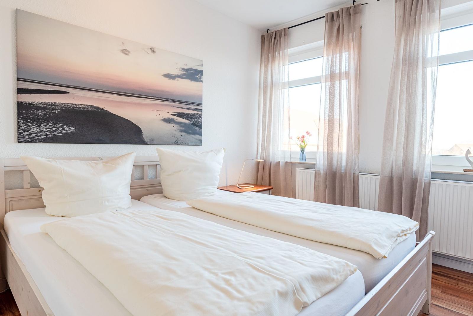 Zimmer mit Doppelbett, Fenster und Wandbild. Vorhänge und Holzboden.