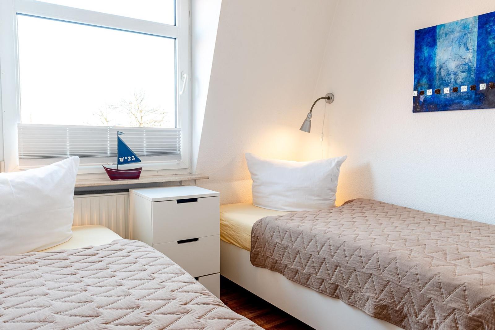 Zwei Betten mit Decken, Nachttisch und Wandlampe. Fenster mit Jalousie und Segelboot.