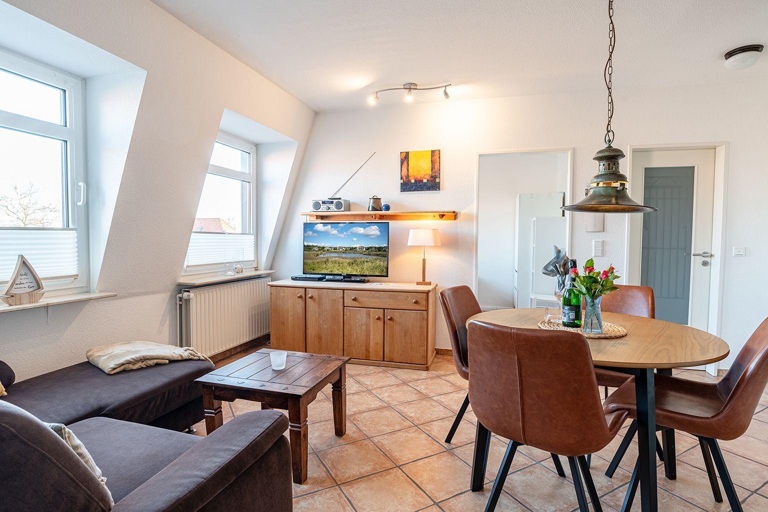 Wohn- und Essbereich mit Holztisch, braunen Stühlen und Fernseher.