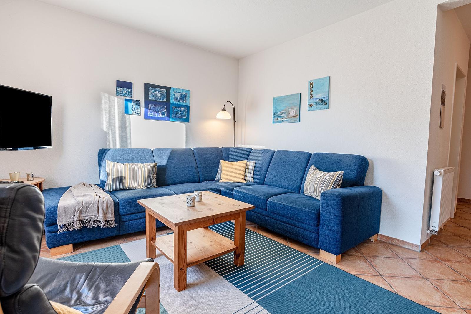 Ein Wohnzimmer mit blauem Sofa, Holztisch und Wandbildern.
