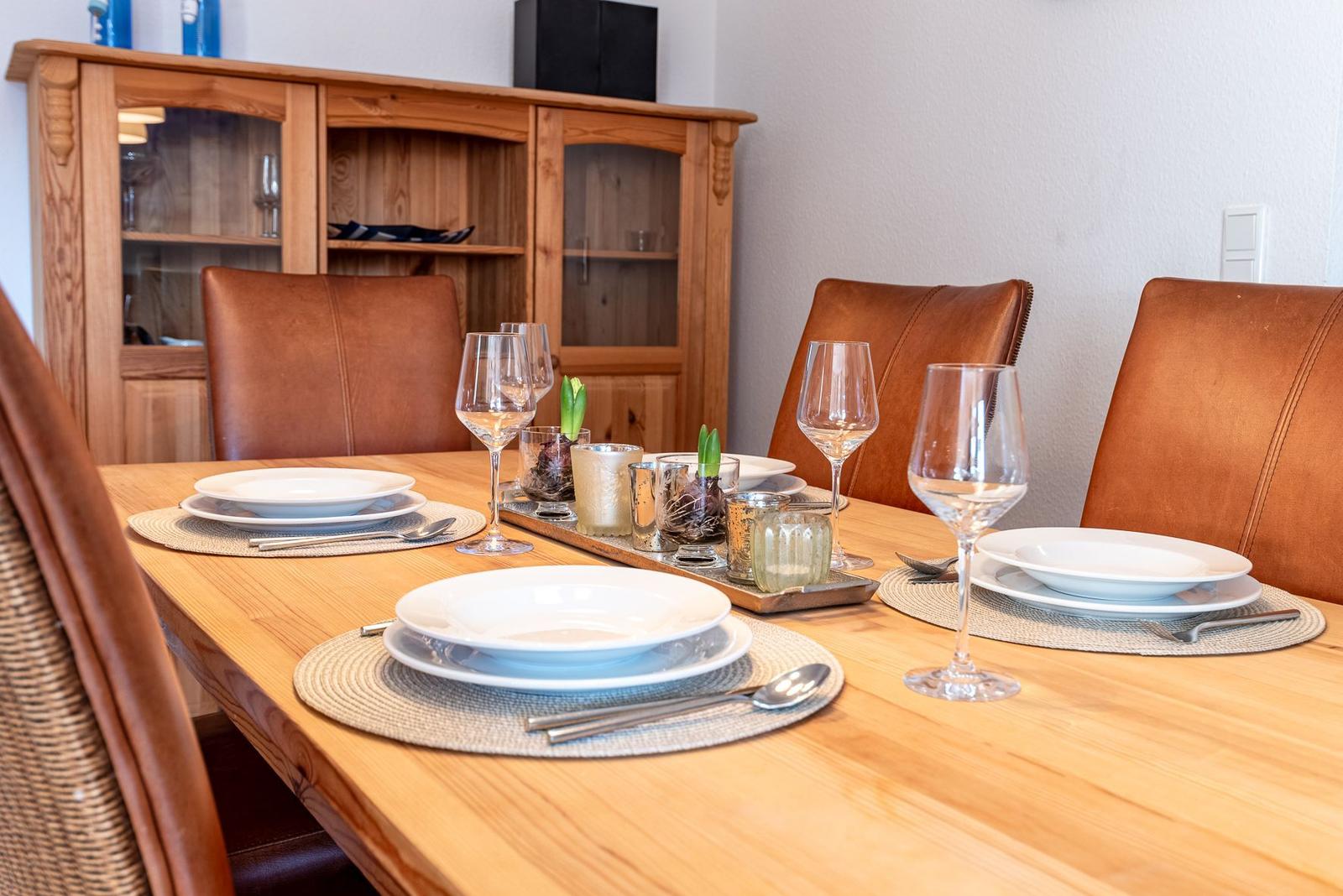 Esstisch mit vier Stühlen, Geschirr und Gläsern. Hintergrund: Holzschrank mit Glasfront.