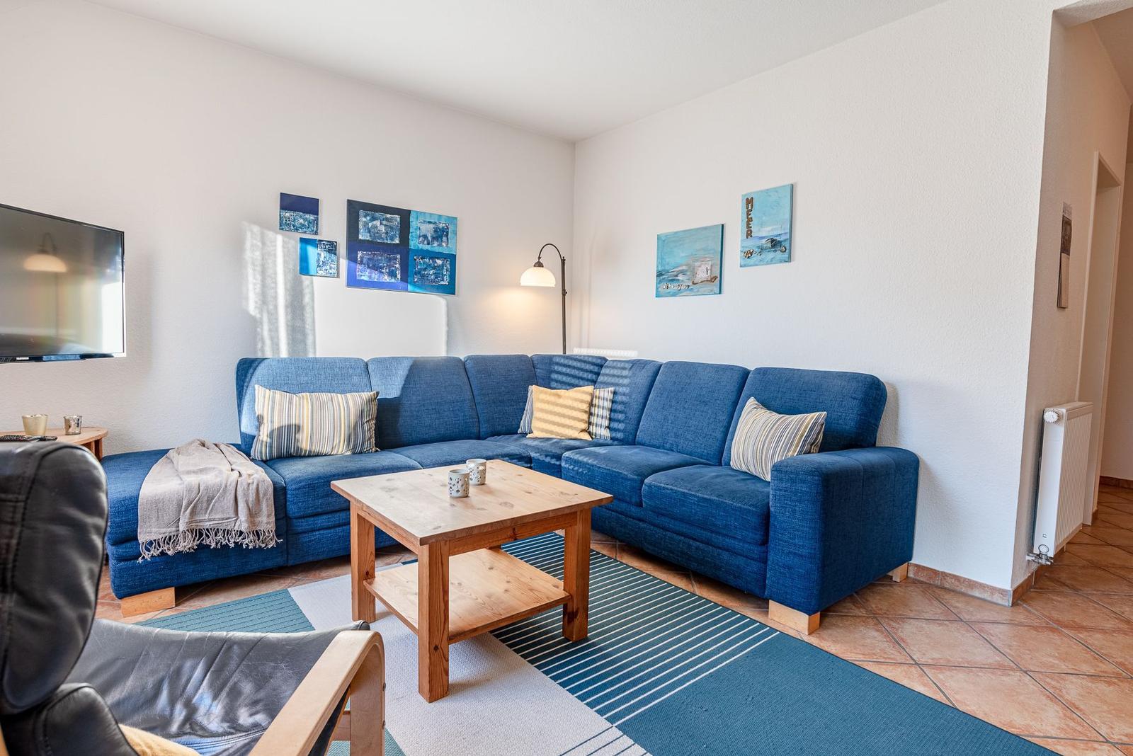 Ein Wohnzimmer mit blauem Sofa, Holztisch und Wandbildern.