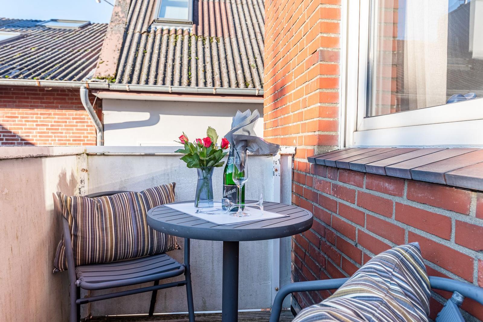 Terrasse mit Tisch, Stühlen und Blumen. Hintergrund: rote Ziegelmauer und Dach.