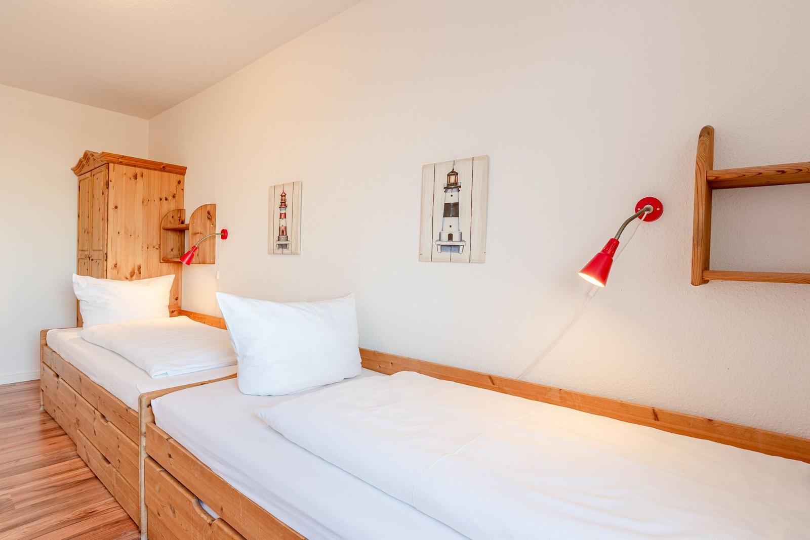 Zwei Einzelbetten mit weißen Bettwäschen und Holzmöbeln an der Wand.