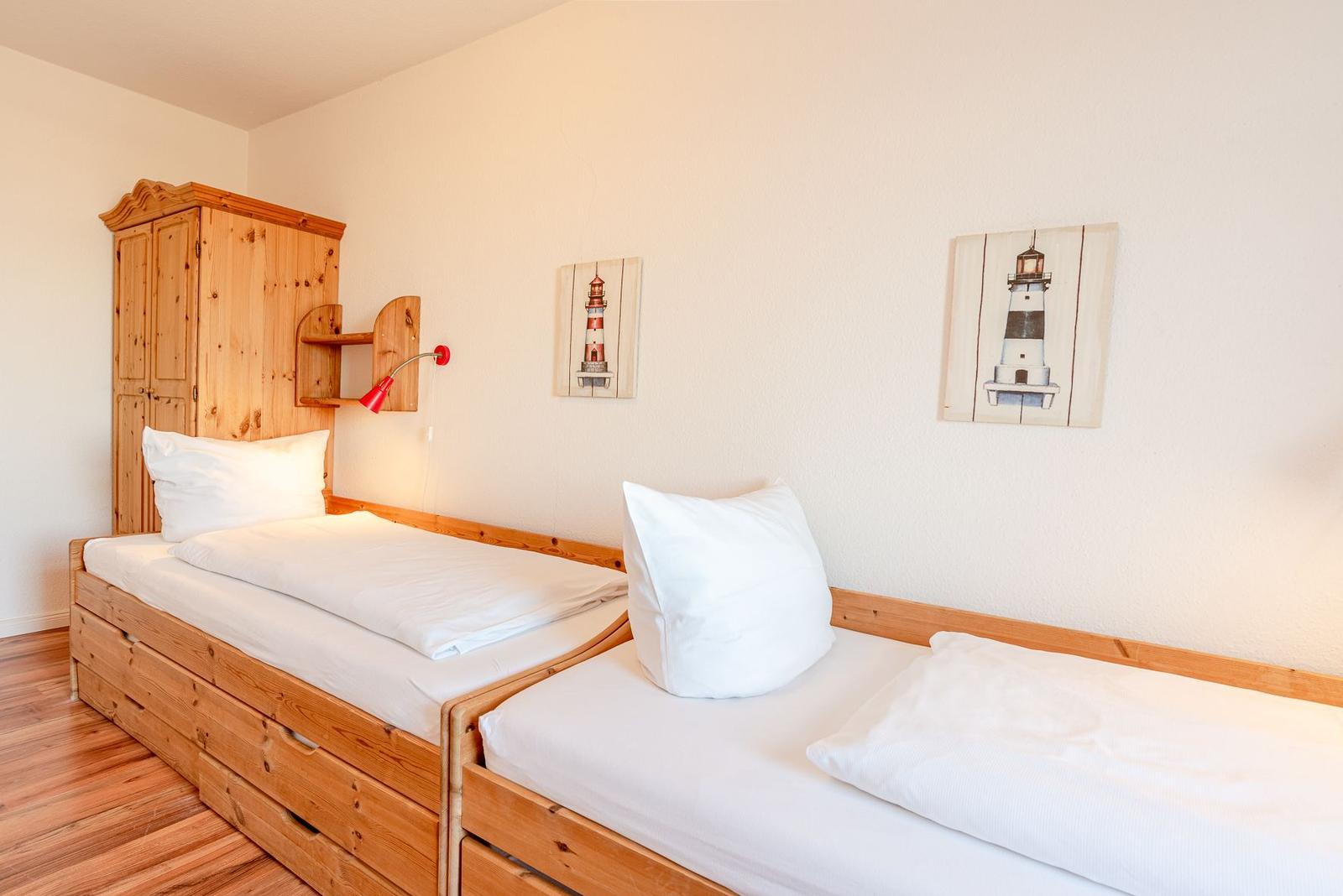 Zwei Betten mit weißen Laken, Holzmöbel und Leuchten an der Wand.
