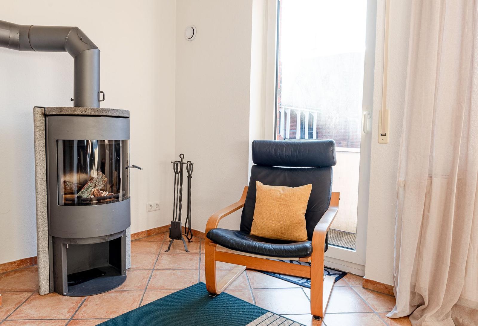 Raum mit Kaminofen, Sessel und Fenster zum Balkon.