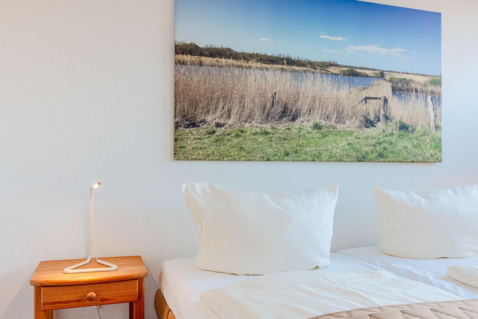 Ein Bett mit weißen Kissen und einer Nachttischlampe neben einem Wandbild.