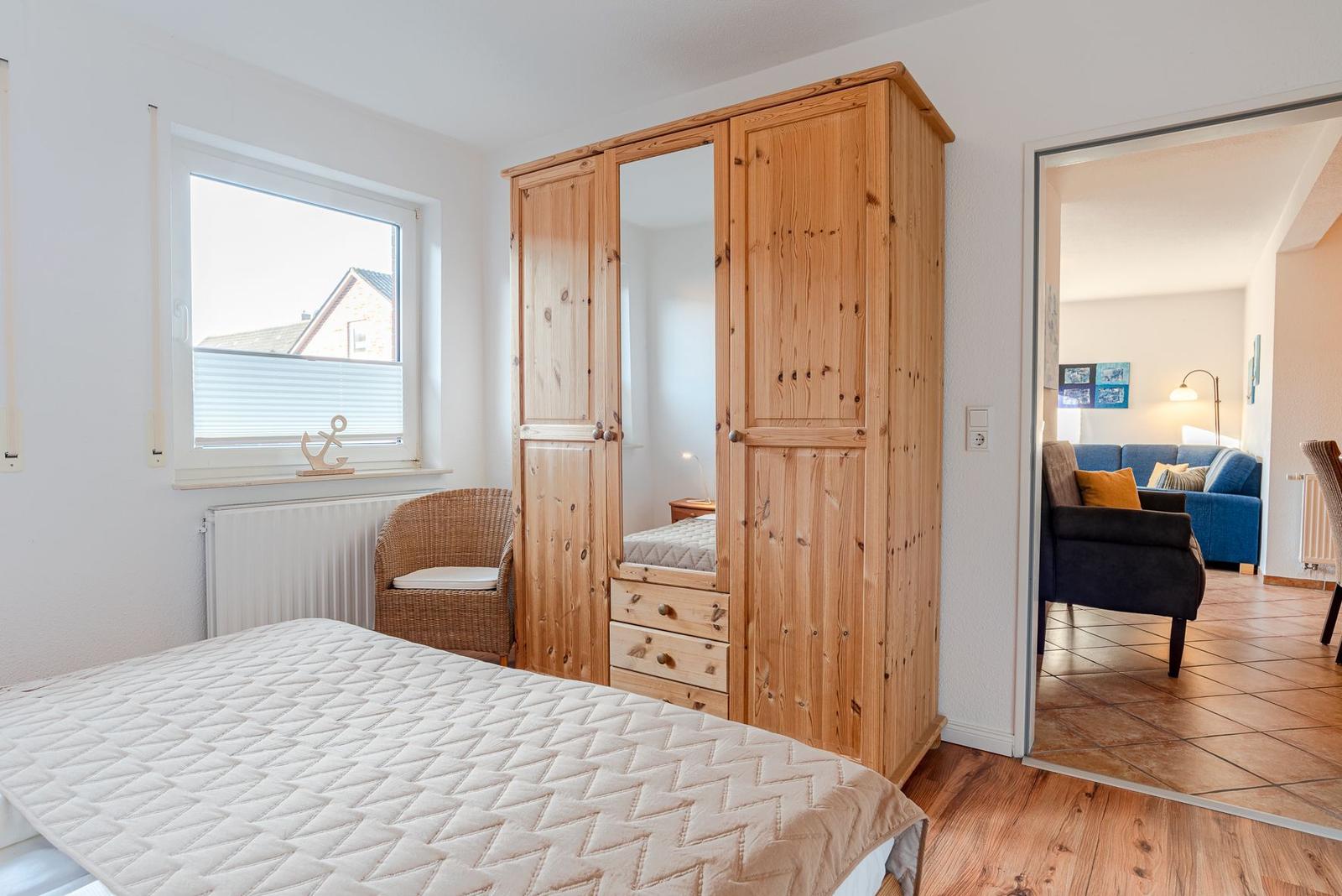 Schlafzimmer mit Holzschrank, Bett und Blick in Wohnzimmer