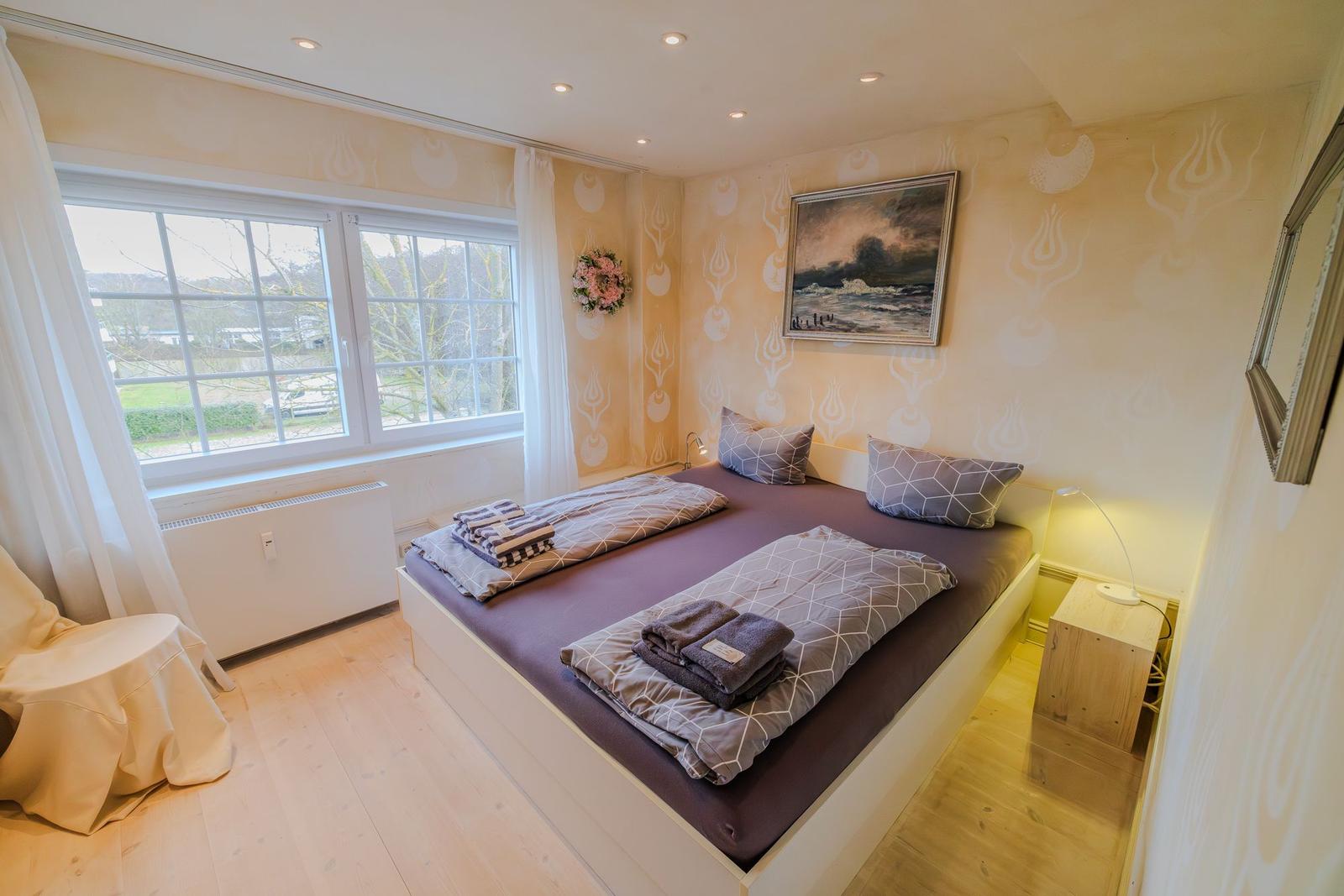 Schlafzimmer mit Doppelbett, Fenster und Wandbild.