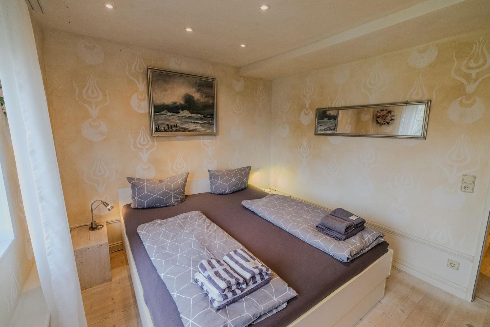Schlafzimmer mit Doppelbett, Wandtapete, Bild und Spiegel.