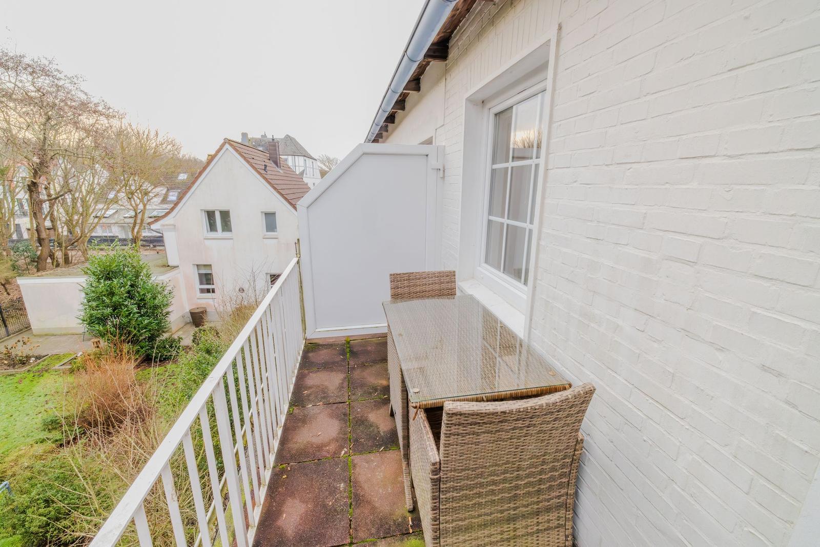 Terrasse mit Tisch und Stühlen, weißer Zaun und Blick auf Garten und Nachbarhaus.