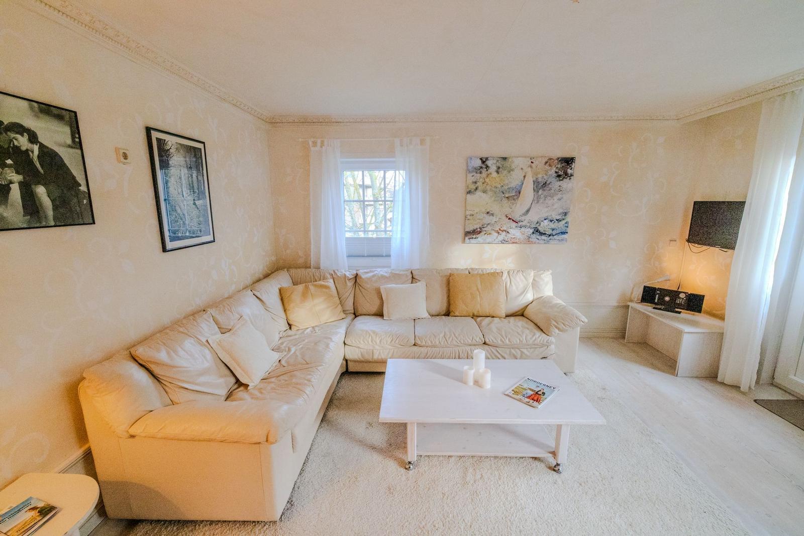 Wohnzimmer mit L-förmigem Sofa, Tisch und Wandbildern.