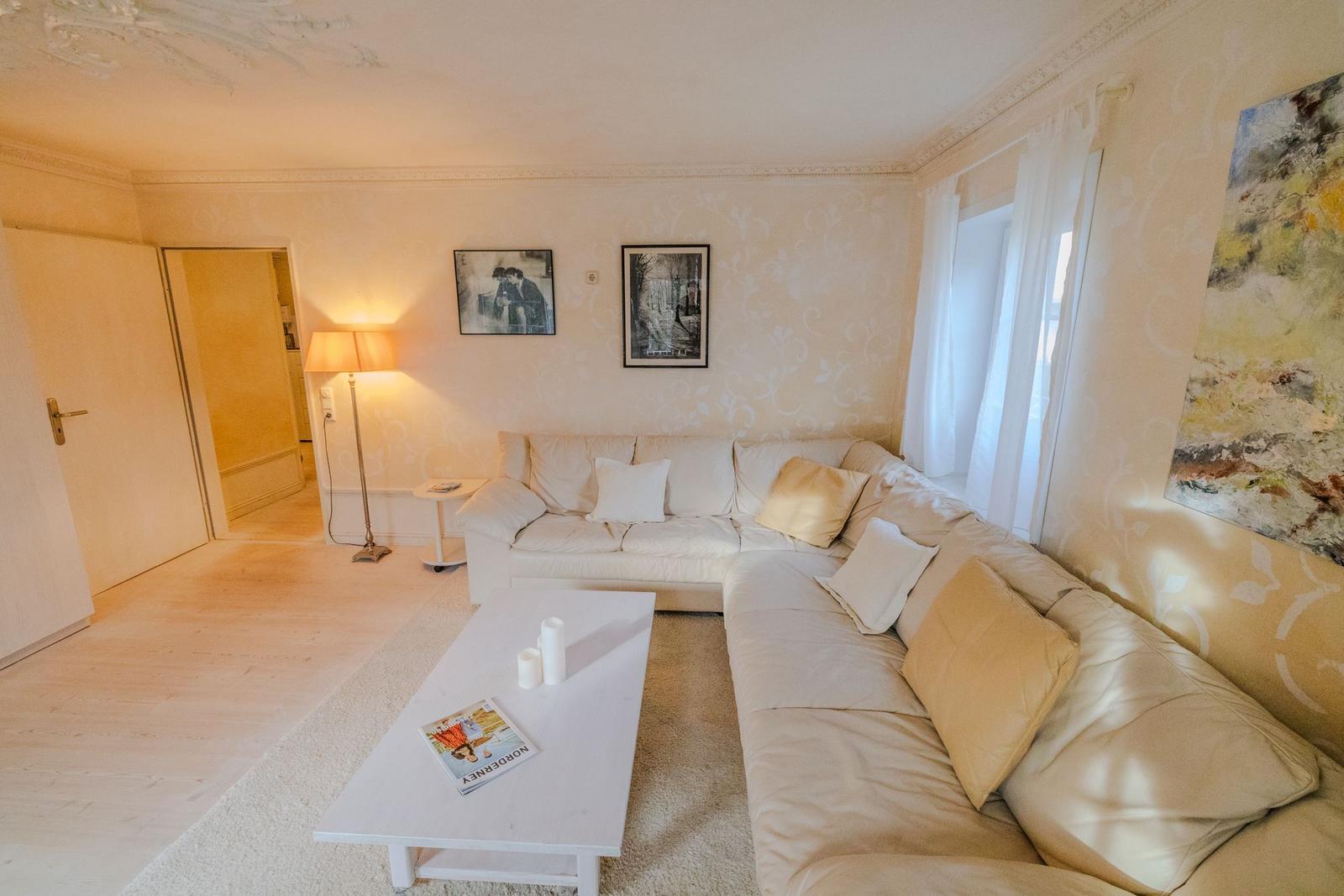 Wohnzimmer mit Ecksofa, Tisch und Wandbildern.