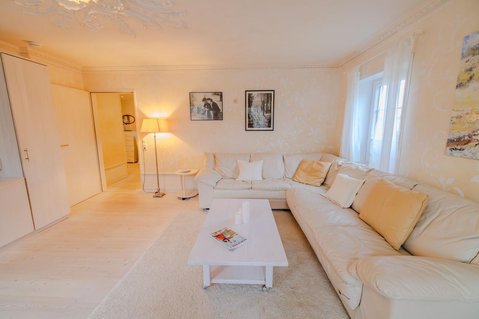 Wohnzimmer mit Ecksofa, Couchtisch und Wandbildern. Decke mit Stuckverzierung.