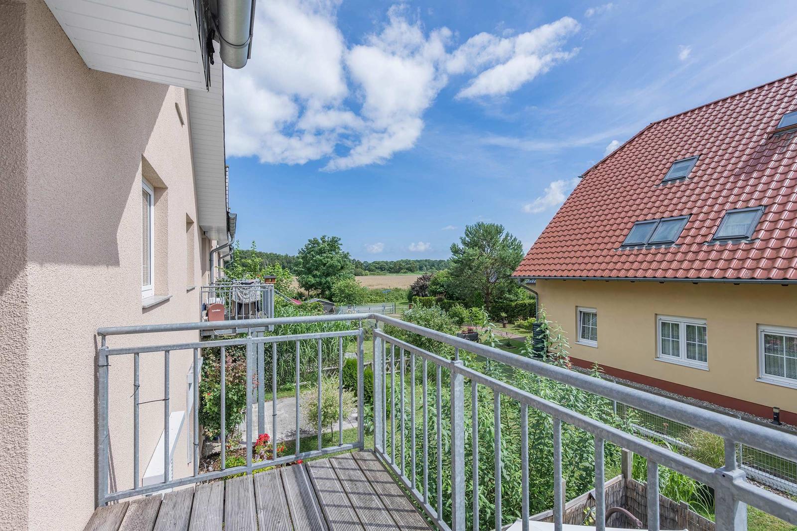 Terrasse mit Blick auf grüne Landschaft und benachbarte Häuser unter blauem Himmel.