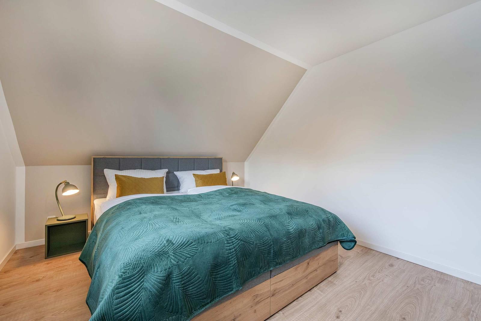 Schlafzimmer mit Dachschrägen, Bett mit grünem Daunendeckel und zwei Nachttischen.