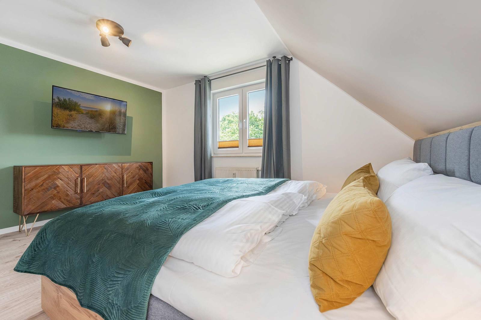 Schlafzimmer mit Doppelbett, Fenster und Fernseher an der Wand.