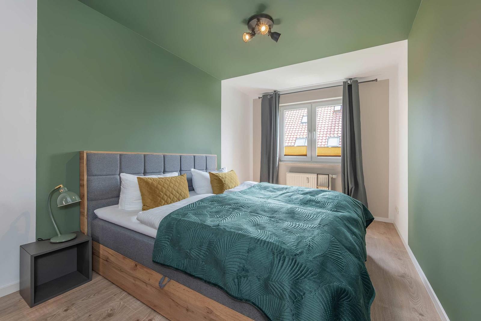 Schlafzimmer mit Bett, grüner Wand und Fenster.