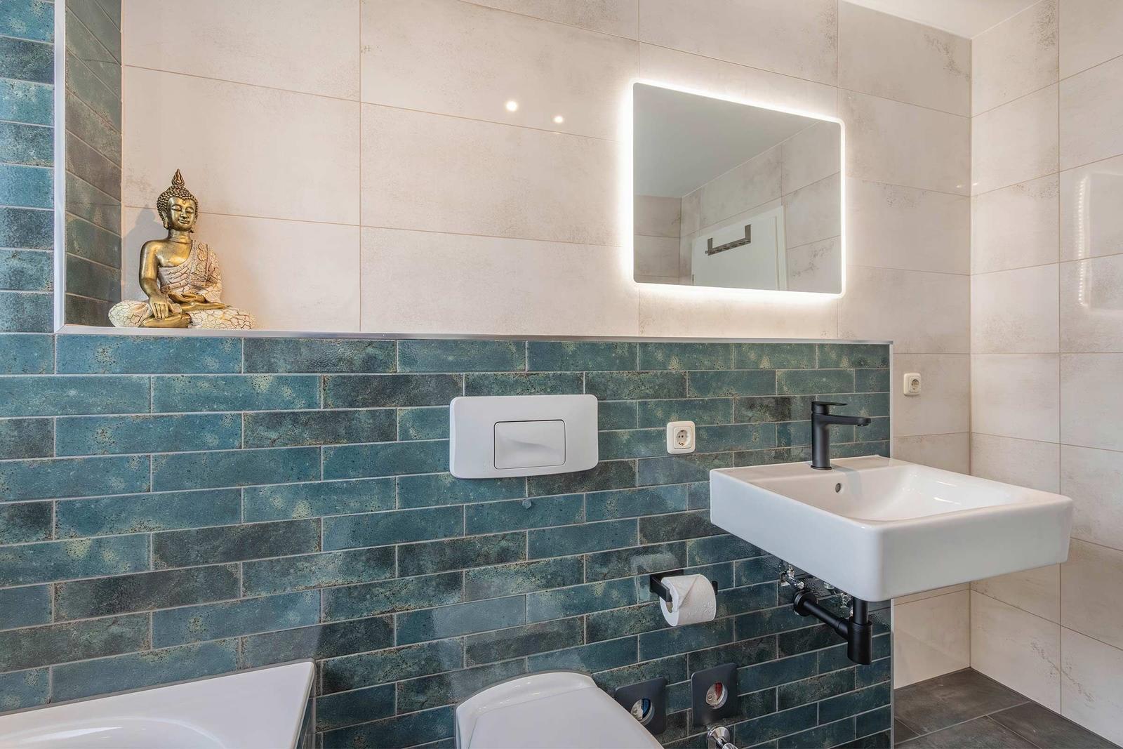 Bad mit Waschbecken, Spiegel und Buddha-Figur an der Wand.