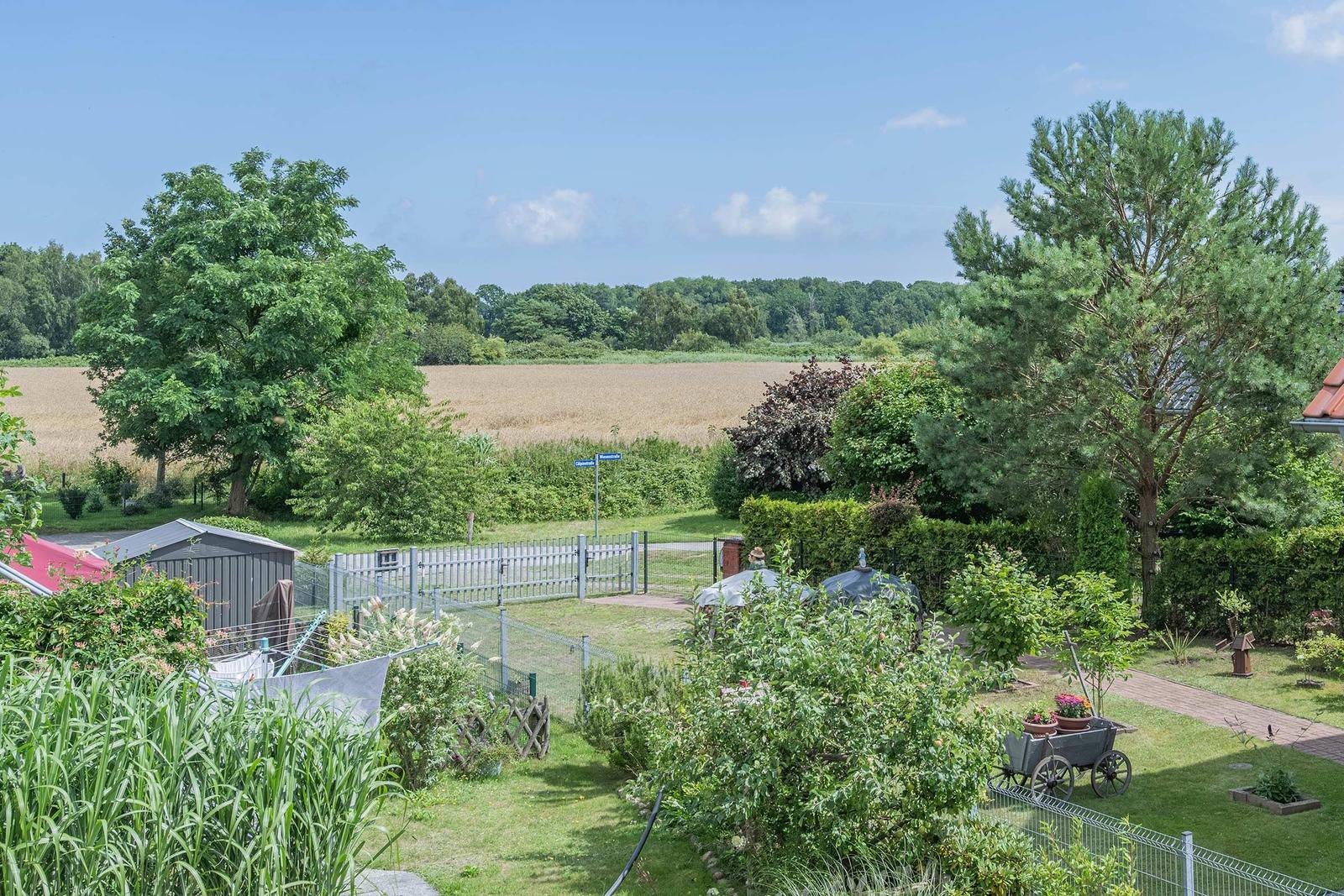 Garten mit Grill, Pflanzen und Blick auf Felder und Bäume.