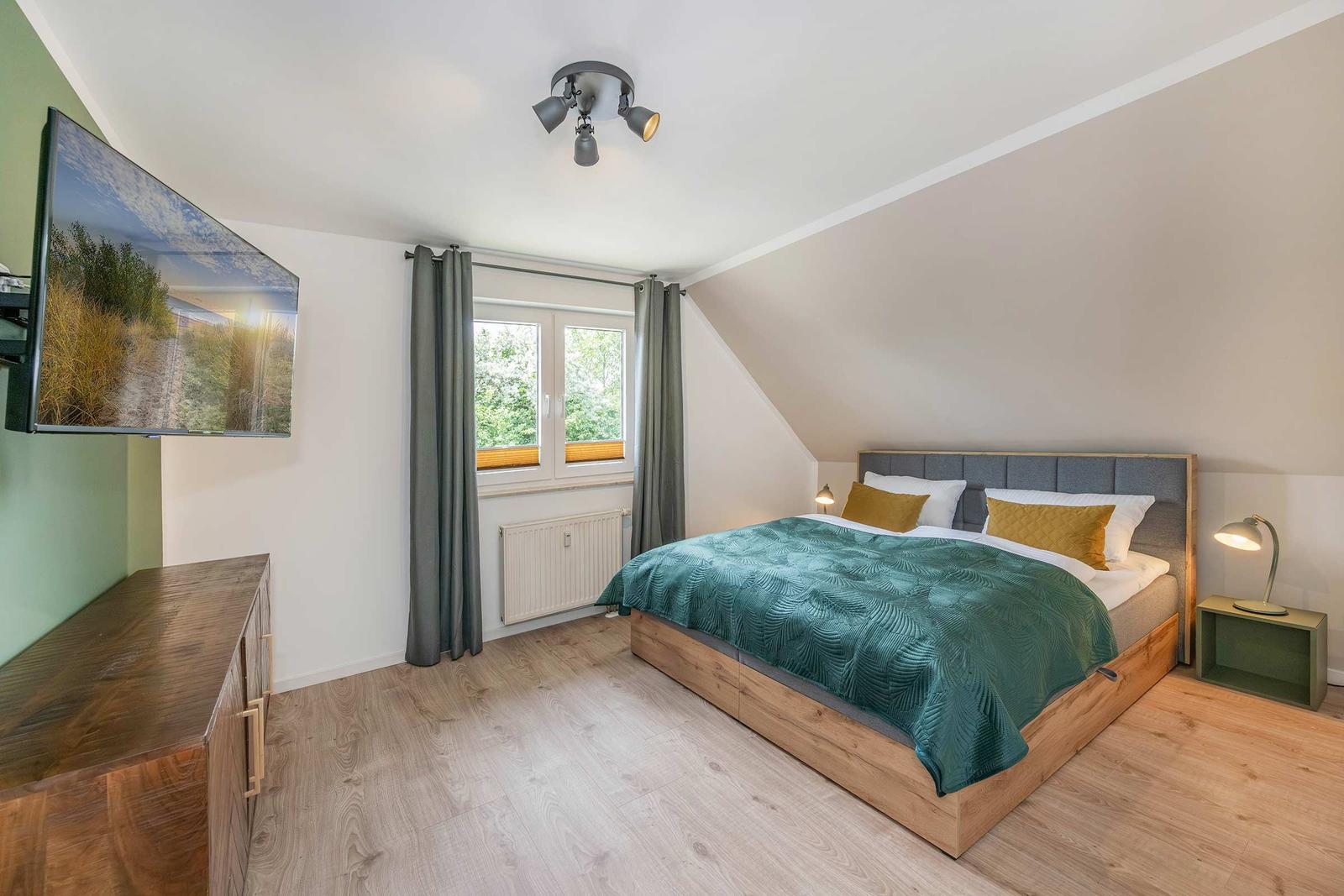 Schlafzimmer mit Bett, Fenster, TV und Nachttisch.