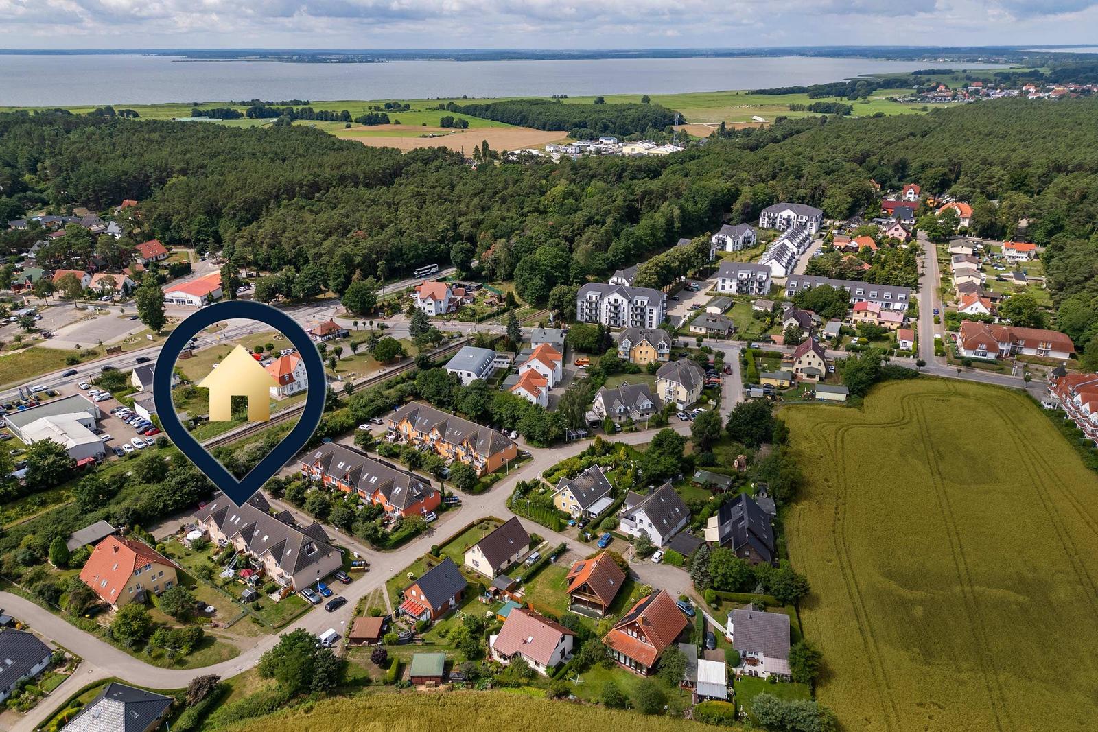 Luftbild eines Dorfes mit Häusern, Wäldern und einem großen See im Hintergrund.