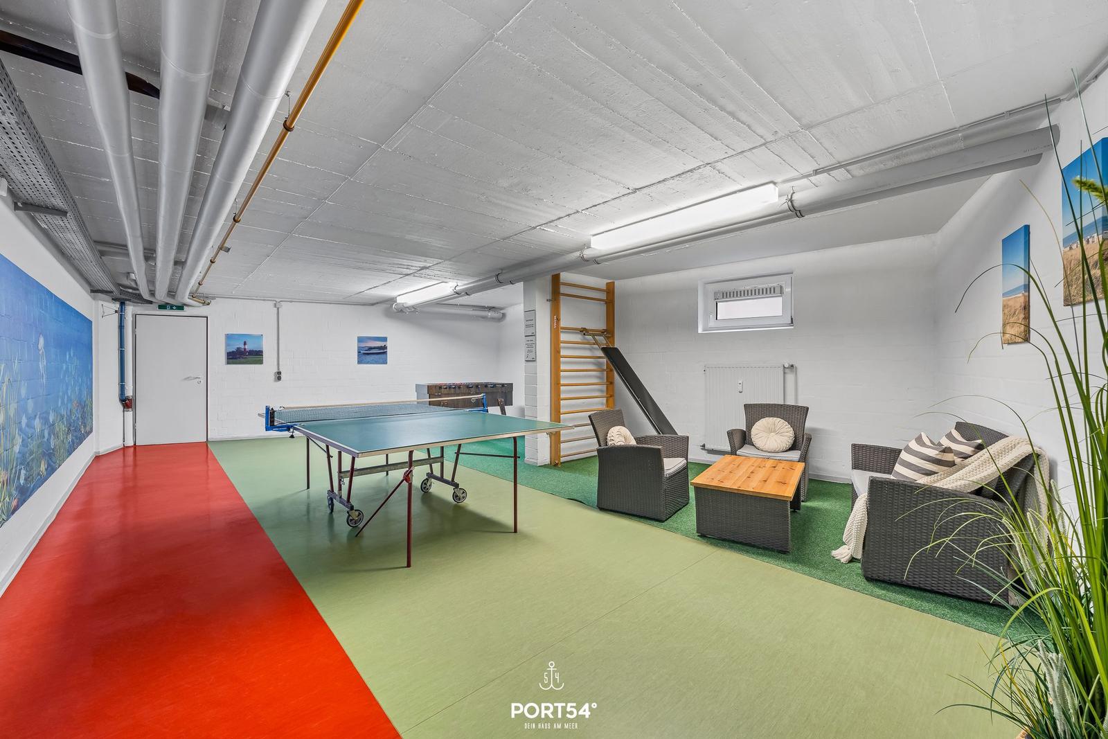 Raum mit Tischtennisplatte, Sitzgruppe und Klettergerüst. Boden rot und grün. Decke mit Rohren.