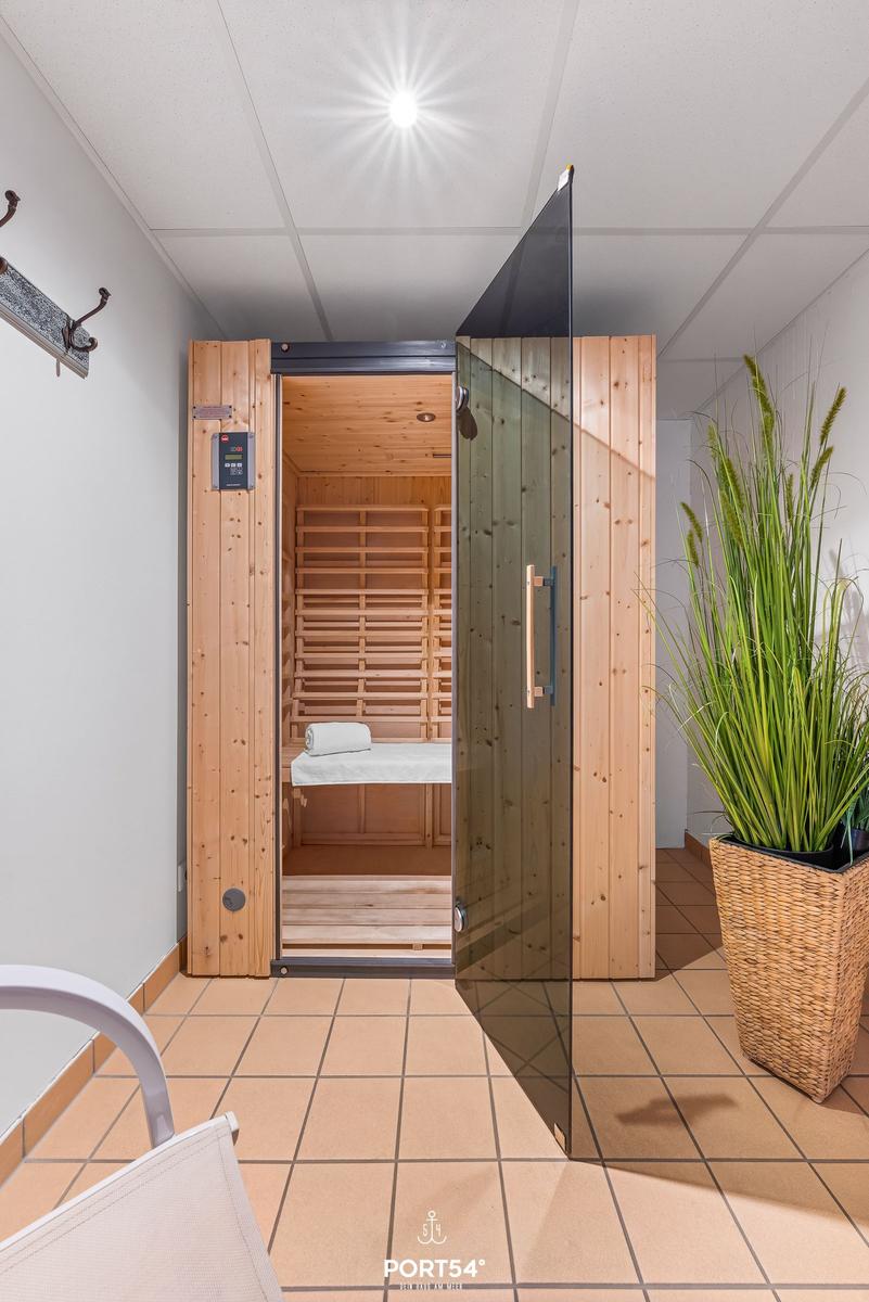 Sauna mit Holzwand und Glasfront, daneben Pflanze in Korb