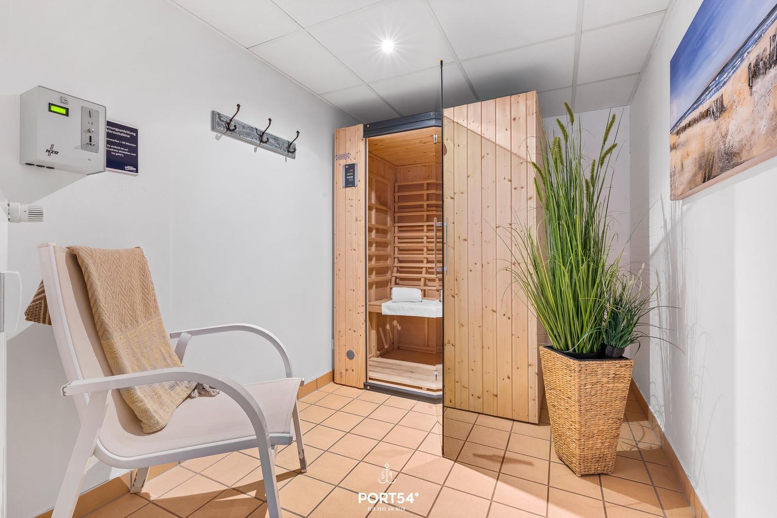 Sauna mit Holzverkleidung und Sitzbank. Weiße Sitzgelegenheit und Pflanze im Vordergrund.