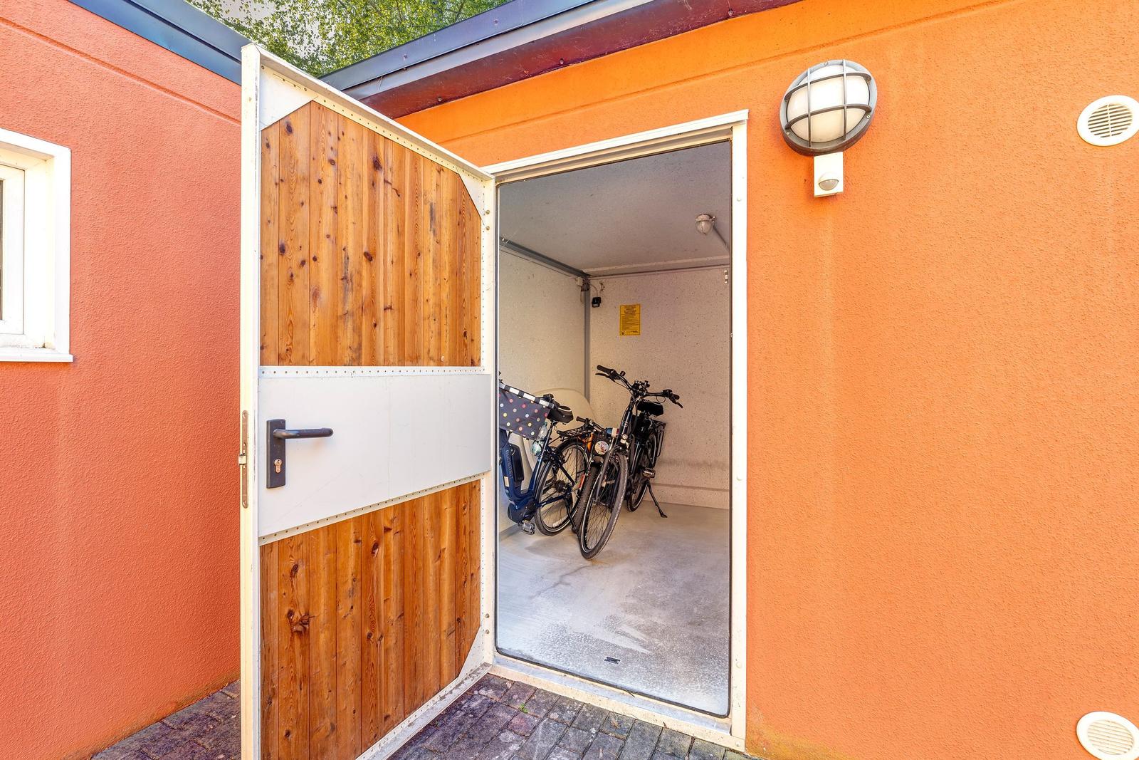 Eingangstor zu einer Garage mit Fahrrädern und Außenbeleuchtung an orangefarbener Wand.