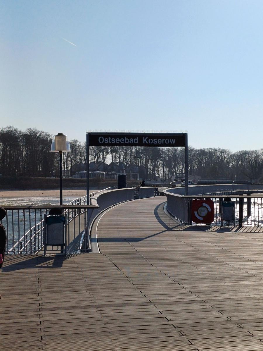 Holzpromenade führt zum Ostseebad Koserow. Sichtbar sind Geländer, Leuchten und ein Rettungsring.