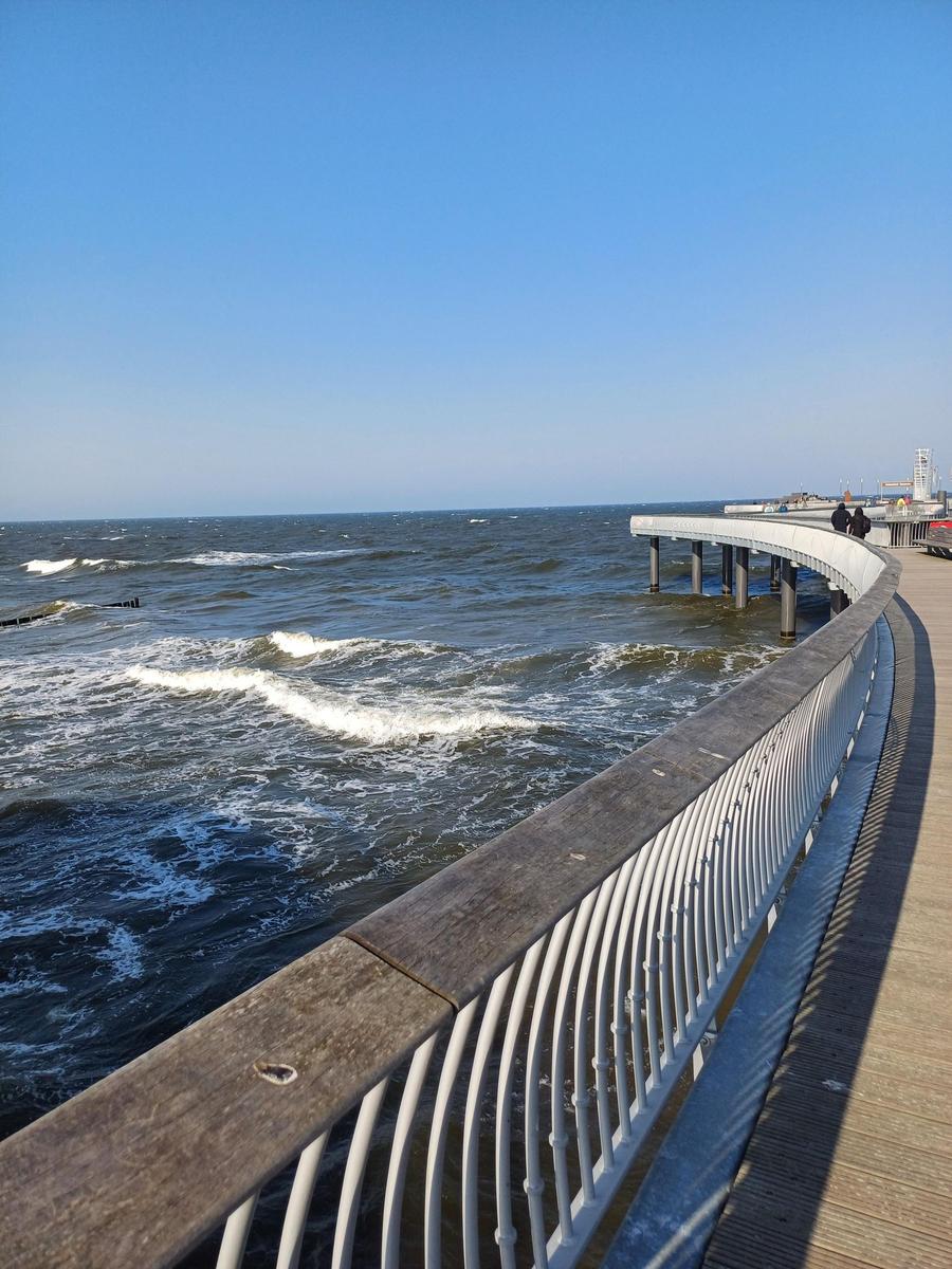 Holzpromenade mit weißem Geländer und Blick auf das Meer.