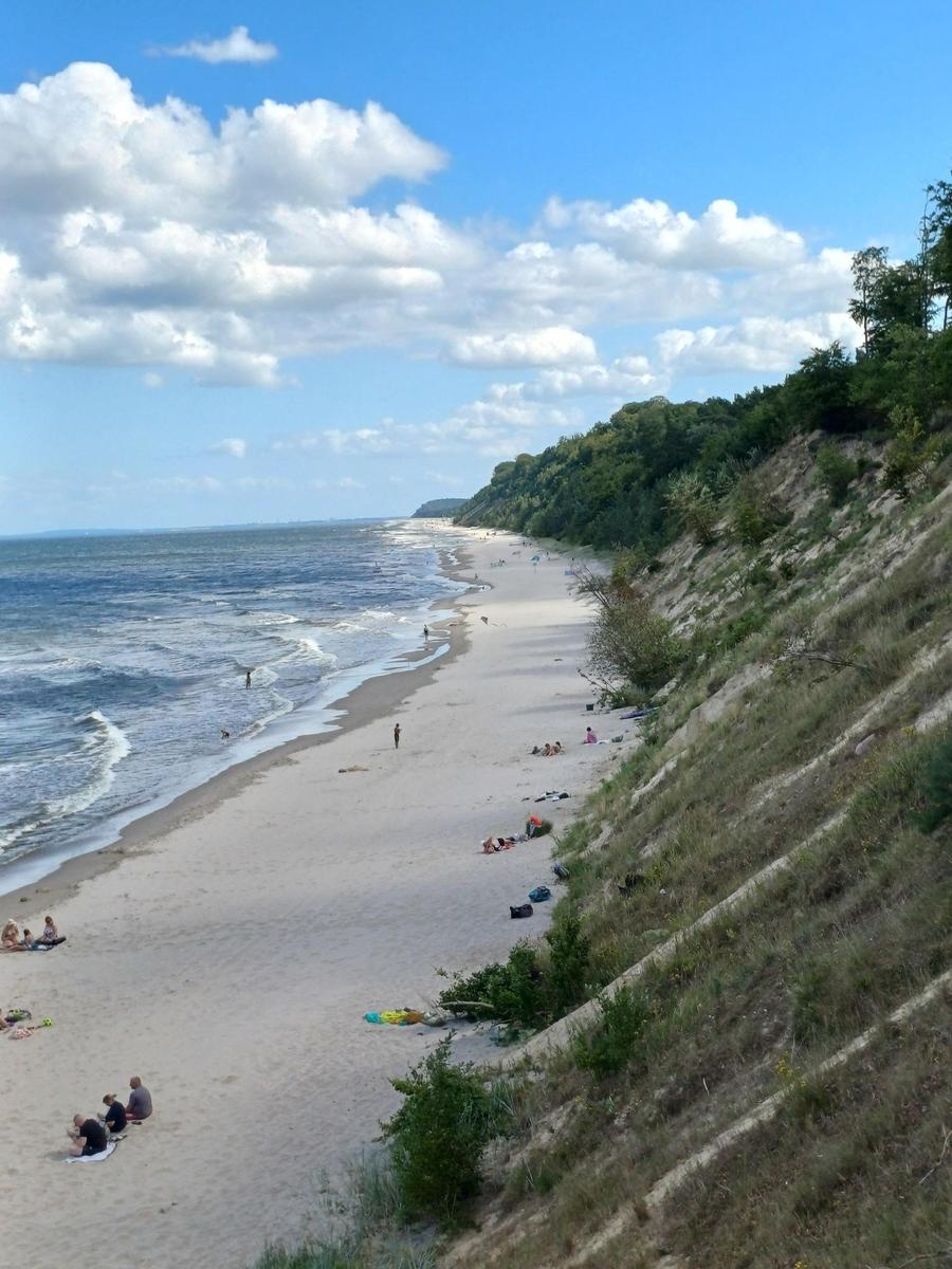 Strand mit Sand und Meer unter blauem Himmel mit weißen Wolken.