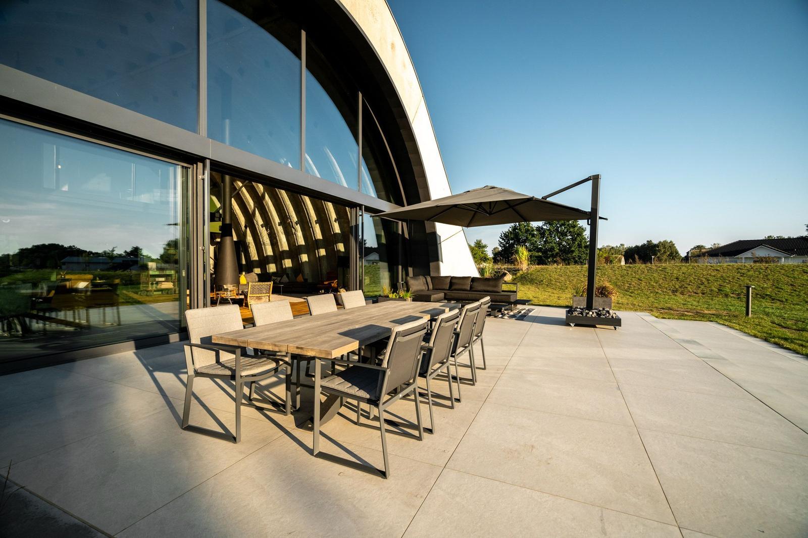 Außenbereich mit Tisch, Stühlen und Sonnenschirm vor modernem Haus.