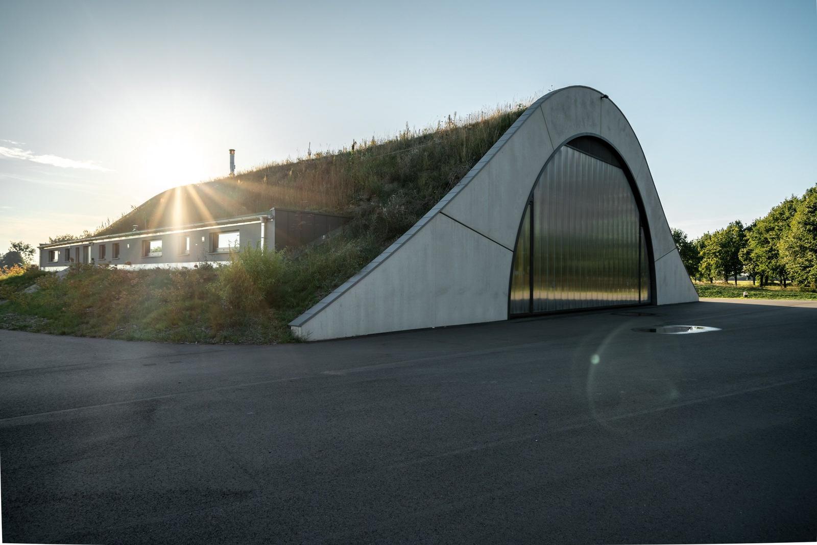 Moderne Architektur mit grüner Dachfläche und großem Tor. Sonne scheint, asphaltierter Platz.
