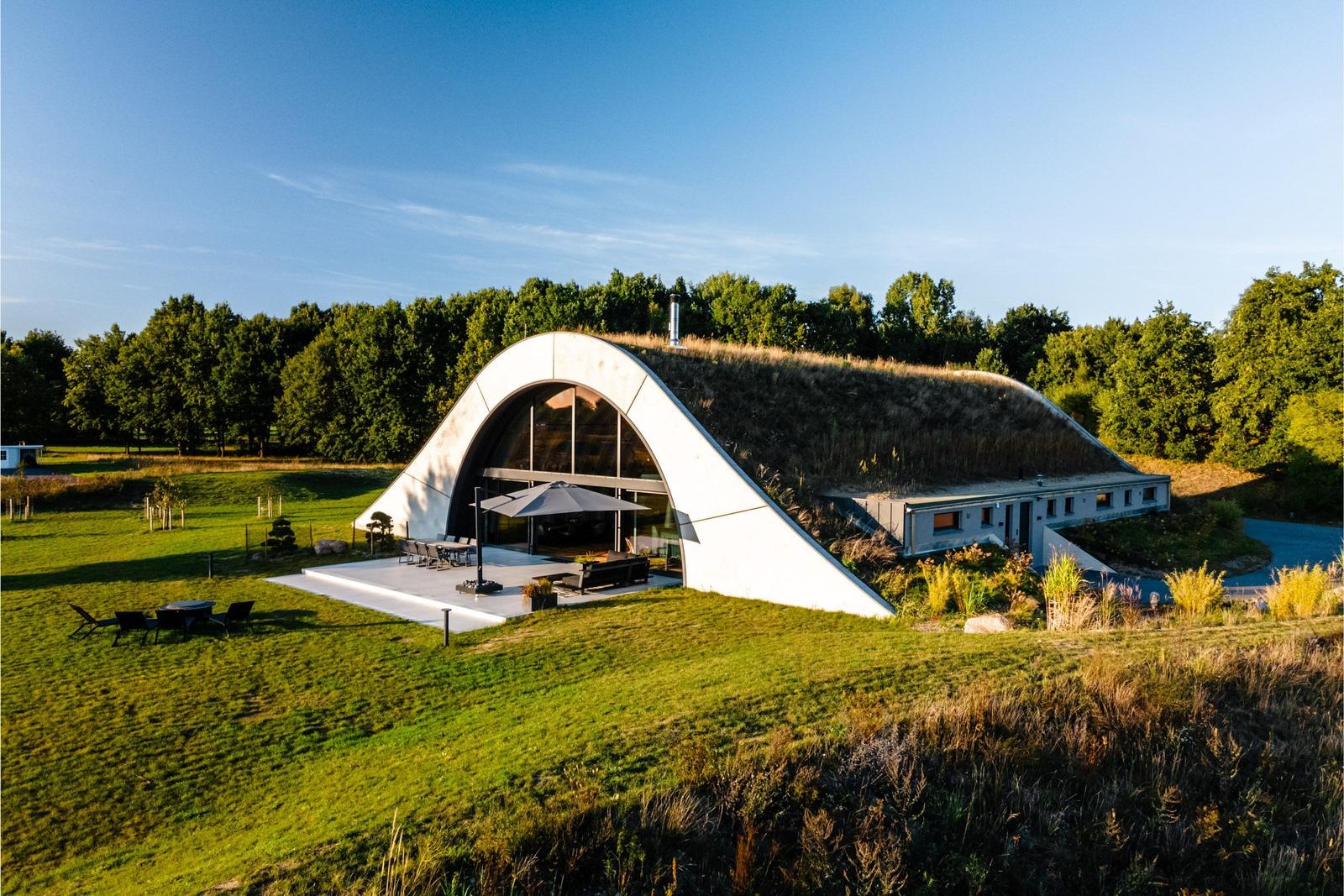 Moderne Architektur mit grünem Dach, Terrasse und Garten. Umgeben von Wald und Grasland.