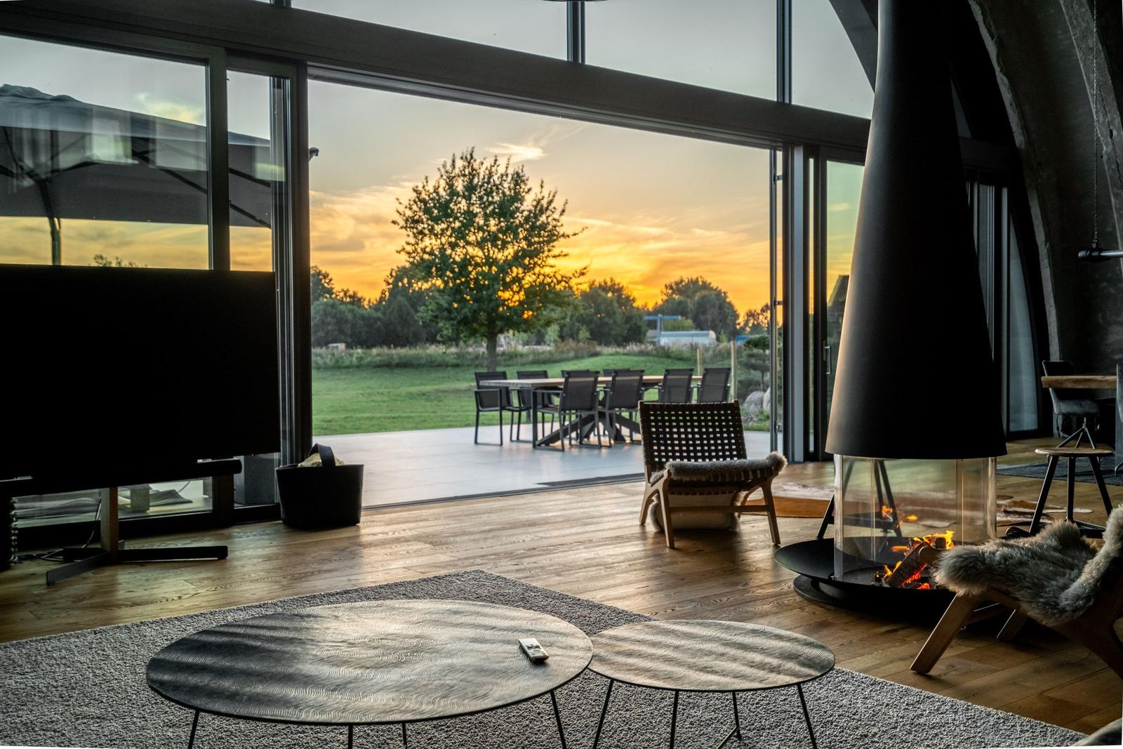 Großes Wohnzimmer mit Kamin und Blick auf Garten bei Sonnenuntergang.