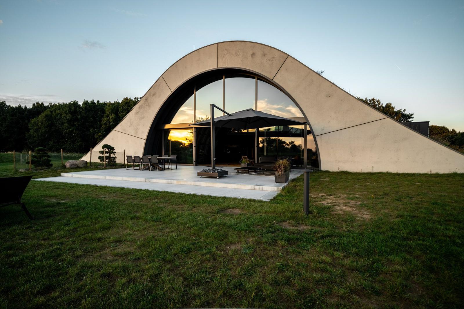 Moderne Architektur mit großem Glasbereich und Terrasse mit Sitzgelegenheiten.