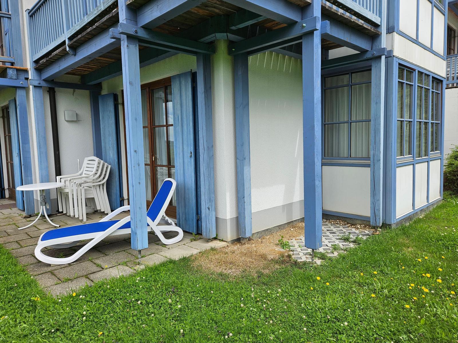 Terrasse mit Liegestuhl und Tisch unter blauem Holzvordach.