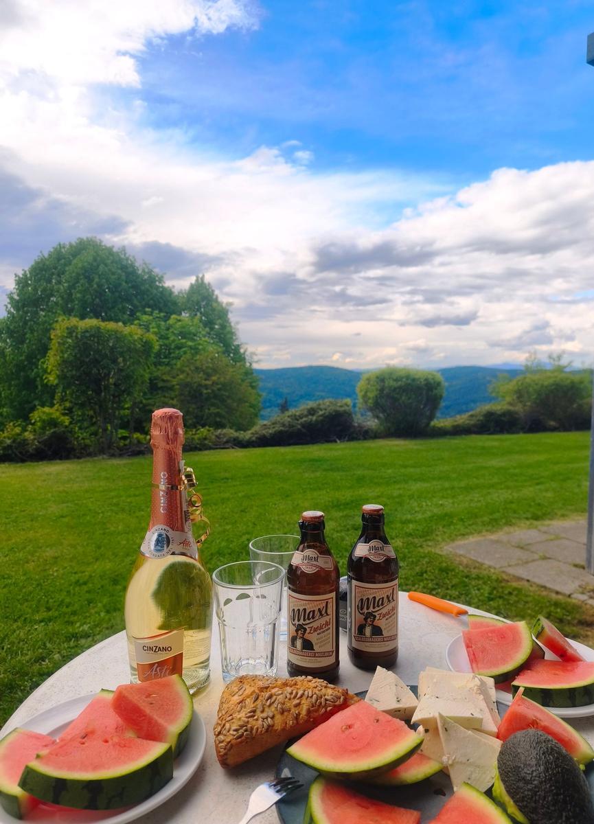 Tisch mit Wassermelone, Bier und Champagner im Garten mit Blick auf grüne Landschaft.