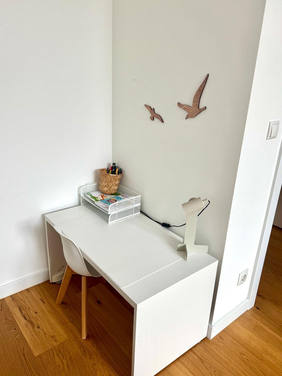 Ein weißer Schreibtisch mit Stuhl, Lampe und Dekoration an der Wand.