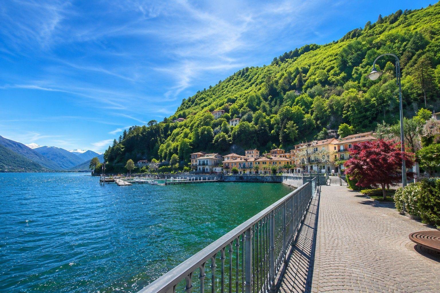 Wasseruferpromenade mit Blick auf grüne Berghänge und Gebäude entlang des Sees.
