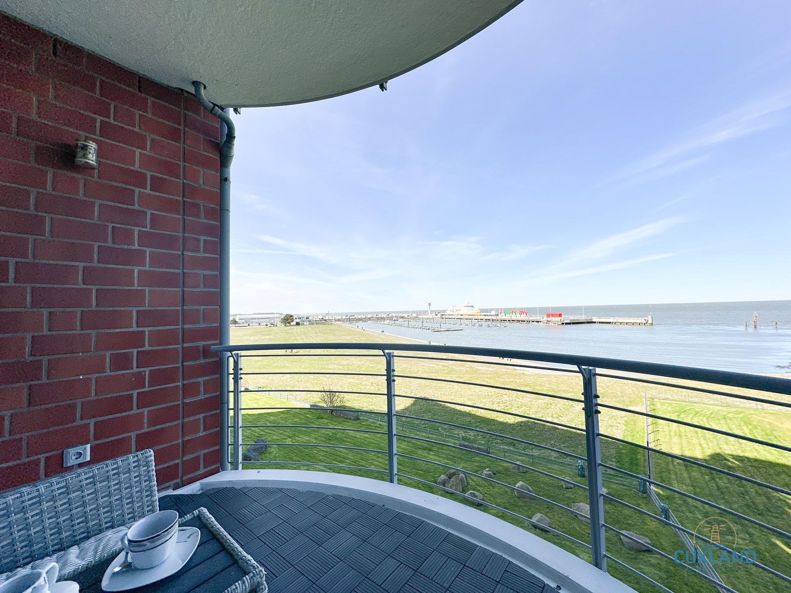 Terrasse mit Blick auf Hafen und Strand. Roter Backstein, Metallgeländer, Tisch mit Tasse.